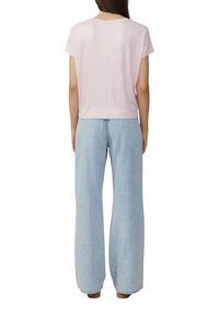 Lichtroze top met korte mouwen en een rechte snit, gecombineerd met lichtblauwe high-waisted wijde jeans. Zichtbare naaddetails op de top.