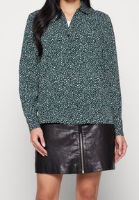 Camicia verde a maniche lunghe con colletto e pois bianchi, abbinata a una mini gonna in pelle nera con zip.
