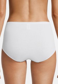 Frau trägt schlichte weiße hochgeschnittene Baumwollunterwäsche, von hinten vor einem einfachen hellen Hintergrund gezeigt.