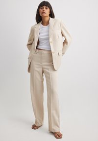 Beige tailored suit with a notched lapel blazer and matching wide-leg trousers. Smooth fabric with buttons and subtle pocket detailing.