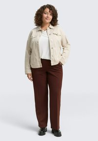 Veste en denim beige, chemise blanche, pantalon marron et bottes noires. La veste possède des poches avant et une fermeture à boutons, avec une coupe décontractée.