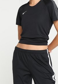 Czarna sportowa koszulka z krótkimi rękawami i zaokrąglonym dekoltem, zestawiona z czarnymi spodniami dresowymi z białymi paskami po bokach i elastycznym pasem.