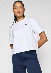 Λευκό κοντό t-shirt από βαμβάκι, με λεπτό μοτίβο και πράσινο λογότυπο στο αριστερό στήθος. Κοντά μανίκια, άνετη εφαρμογή.