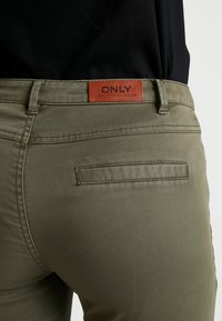 Olive green pants made of cotton blend, featuring a leather brand patch labeled "ONLY" at the waistband and a single back pocket.