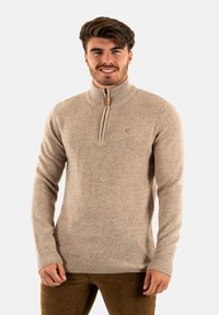Pull en tricot beige avec un col montant, zip demi-long, poignets et ourlet côtelés. Présente un petit logo sur le côté gauche.