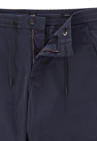 Navy tapered fit pants made of smooth fabric with a zippered fly, button closure, and drawstring; features minimal stitching details.