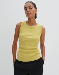 Top leggero giallo chiaro a coste senza maniche con scollatura rotonda. Abbinato a pantaloni neri larghi. Design minimalista, texture liscia.