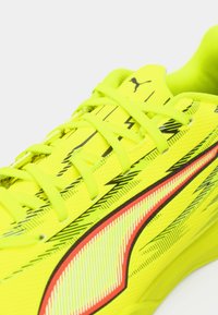 Neongule sportssko med tekstureret syntetisk overdel, sorte zigzag-mønstre og røde accenter langs siderne. Snørebåndene er lysegrønne.