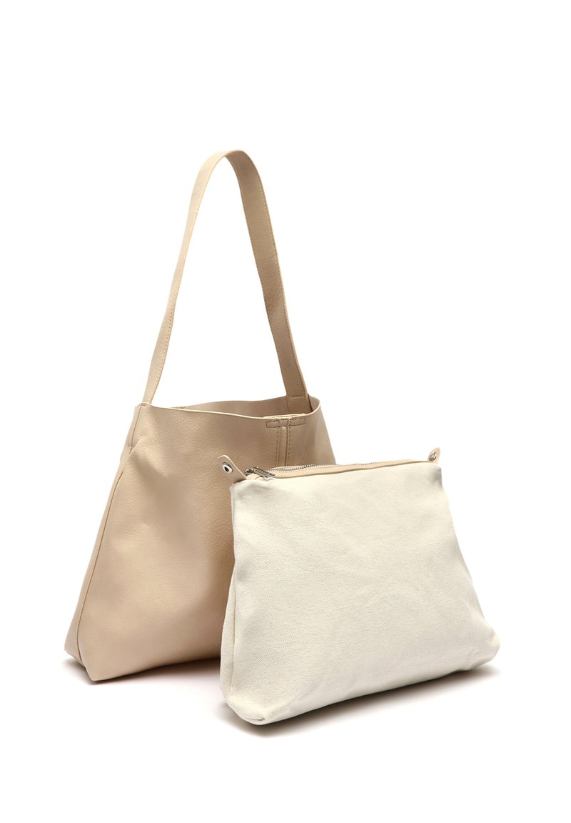 Beige nahka-tote-laukku, jossa on sileä pinta ja kaksi pitkää kahvaa. Edessä on pienempi valkoinen kangaspussukka, jossa on vetoketju.