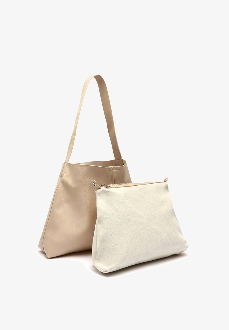 Beige nahka-tote-laukku, jossa on sileä pinta ja kaksi pitkää kahvaa. Edessä on pienempi valkoinen kangaspussukka, jossa on vetoketju.