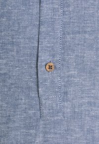 Zbliżenie niebieskiego, teksturowanego materiału z pojedynczym małym brązowym guzikiem przyszytym do pionowego szwu.