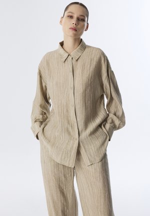 Camisa de rayas beige con cuello tipo polo, botón en la parte frontal y corte relajado. La tela presenta sutiles texturas irregulares y detalles.