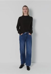 Czarny sweter z długim rękawem, luźny krój. Niebieskie dżinsy z szerokimi nogawkami, średnie przetarcie, lekko wypłowiałe. Czarne botki za kostkę, gładka tekstura.