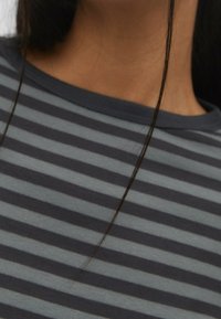 Gros plan sur le cou et le haut de la poitrine d'une personne portant une chemise rayée gris foncé et gris clair, avec deux mèches de cheveux foncés tombant vers l'avant.