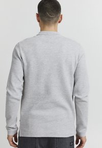 Graues Langarmshirt aus strukturiertem Strickstoff mit Rundhalsausschnitt und Seitenschlitzen. Das Shirt wird mit dunkelgrauen Hosen kombiniert.