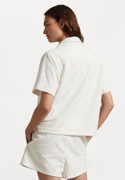 Chemise blanche texturée à manches courtes avec un motif géométrique, assortie à un short. Comprend une coupe décontractée et des détails au niveau du col.
