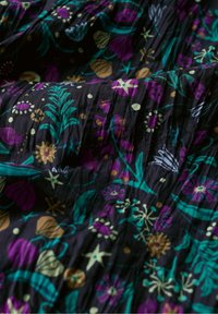 Tessuto nero con un motivo floreale in viola, turchese e oro. Texture a pieghe, con diverse forme di fiori e foglie.