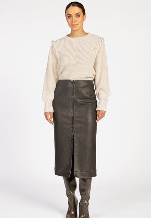 Beige gebreide trui met een gestructureerde schouderafwerking, gecombineerd met een hooggetailleerde zwarte leren kokerrok met een voorrits en een split.