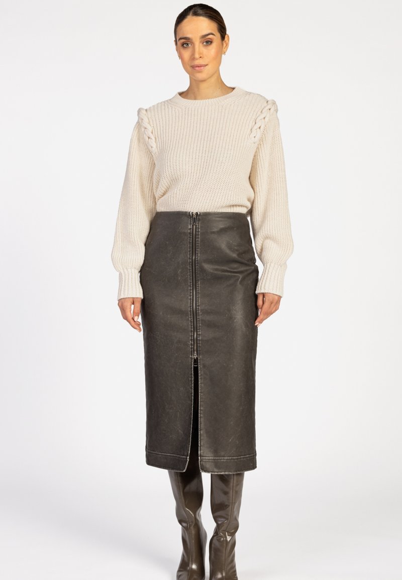 Beige gebreide trui met een gestructureerde schouderafwerking, gecombineerd met een hooggetailleerde zwarte leren kokerrok met een voorrits en een split.