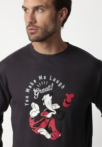 Sudadera negra con un gráfico de un personaje de perro de dibujos animados, con acentos rojos y blancos. El texto dice "¡Me haces reír mucho!"
