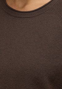 Gros plan d'une personne portant un pull marron uni en maille avec un col côtelé.