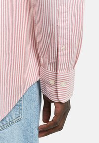 Röd- och vitrandig skjorta med knapp-manschetter, tillverkad av lättviktig tyg, med rundad fåll och synliga sömdetaljer.