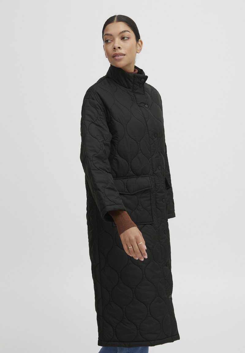 Abrigo largo acolchado negro con cuello alto, que cuenta con un cierre de botones y bolsillos laterales. Fabricado con una tela suave y texturada.
