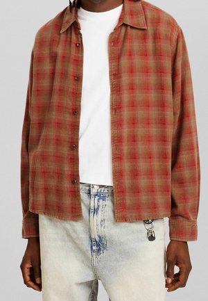 Man wearing a red plaid button-up shirt over a white t-shirt, light blue acid-wash jeans with keychain clipped to belt loop.