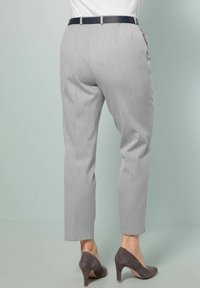 Pantaloni su misura grigio chiaro con una leggera lucentezza, dotati di una vita con una cintura scura e una vestibilità a gamba affusolata fino alla caviglia. Indossati con tacchi grigi.