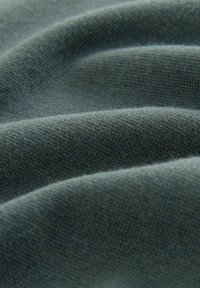 Tissu doux et texturé dans une riche couleur vert foncé avec un motif de tissage visible et un drapé léger, mettant en valeur des contours lisses et fluides.