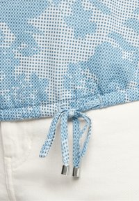 Niebiesko-biała tkanina w kratkę z wzorem, wyposażona w sznurek ze srebrnymi zakończeniami na dole, zestawiona z jasnymi spodniami.