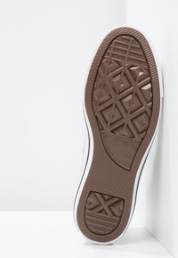 Semelle de basket Converse All Star, présentant une semelle en caoutchouc marron avec un motif géométrique de la bande de roulement et des flancs blancs.