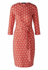 Robe rouge avec un motif de cœur géométrique en crème, manches longues, décolleté arrondi et un détail de taille nouée. Tissu au toucher lisse.