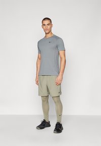 Grå sportt-shirt med svart logotyp, ljusgröna shorts och ljusgröna leggings. Svarta sportskor med strukturerat mönster och gula accenter.