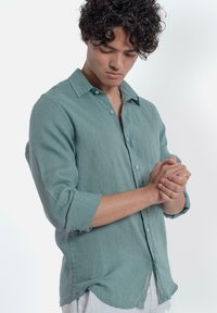 Lichtgroene linnen shirt met lange mouwen, button-down kraag en een ontspannen pasvorm. Geweven stof met subtiele stiksels en een label aan de onderkant.