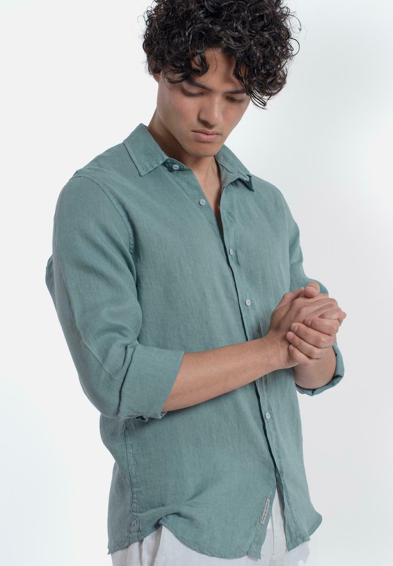 Lichtgroene linnen shirt met lange mouwen, button-down kraag en een ontspannen pasvorm. Geweven stof met subtiele stiksels en een label aan de onderkant.