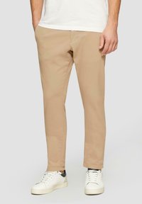 Beige katoenen chinos met een rechte pasvorm, voorzien van zijzakken en een gladde textuur, gecombineerd met witte sneakers.