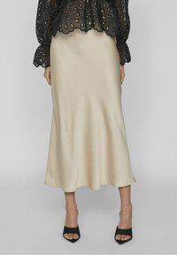 Gonna midi in satin beige con una texture liscia, silhouette fluida e un orlo leggermente svasato, abbinata a décolleté neri con punta aperta.