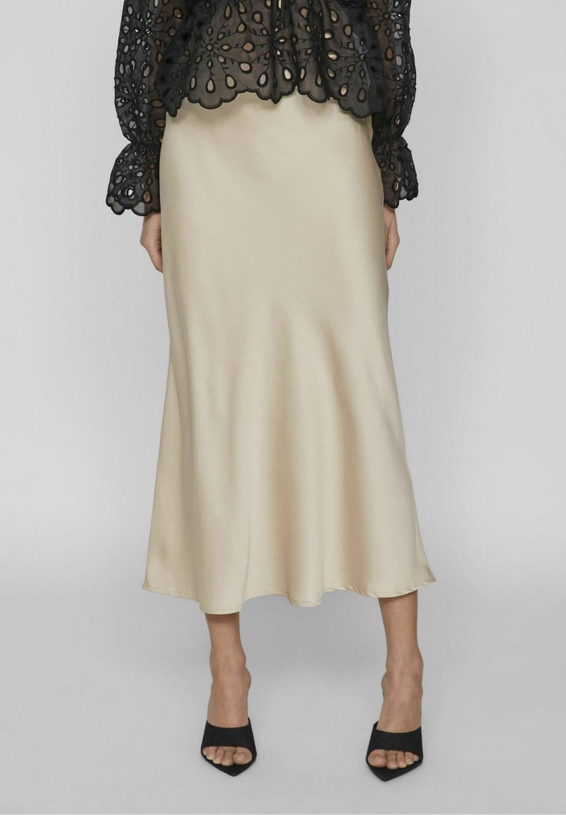 Gonna midi in satin beige con una texture liscia, silhouette fluida e un orlo leggermente svasato, abbinata a décolleté neri con punta aperta.