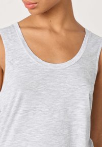 Približna snimka osobe u svijetlosivom topu bez rukava s okruglim izrezom, prikazujući vrat, rame i dio lica.