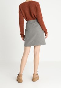 Un pull tricoté de couleur rouille et une jupe en pied-de-poule jusqu'aux genoux, avec des chaussures à plateforme neutres, vues de dos.