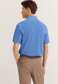 Kurzärmliges Poloshirt aus leichtblauem Stoff mit strukturiertem Kragen. Das Design verfügt über einen geraden Schnitt und eine lockere Passform.