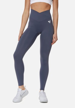 Hoge taille, marineblauwe leggings met een kruislingse ontwerpelement bij de tailleband en een klein wit logo op de linkerdij, gemaakt van gladde, rekbare stof.