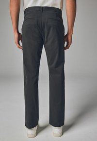 Schwarze Hose mit geradem Bein, aus Baumwollmaterial, und zwei Gesäßtaschen, kombiniert mit weißen Schuhen auf hellem Hintergrund.