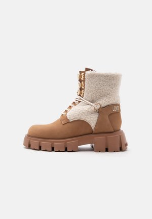 Brown lace-up ankle boot with thick sole and cream-colored fleece lining, featuring gold eyelets and "LOVE" text on the heel strap.