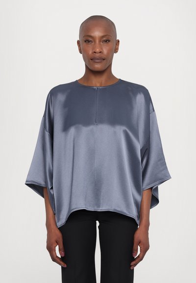 Top oversized din satin gri, cu mâneci scurte, decolteu rotund și un mic placket frontal, asortat cu pantaloni negri. Textură netedă și croială lejeră.