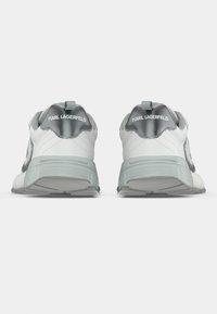 Sportcipők fehér és szürke dizájnnal, texturált bőrrel, hangsúlyos márkajelzéssel és rétegelt díszítéssel ellátott párnázott talppal.