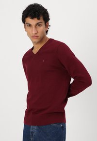 Bordeaux V-hals trui gemaakt van zachte gebreide stof, met lange mouwen, een slim fit en een klein logo-accent op de borst.