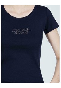 Granatowy t-shirt z krótkim rękawem wykonany z miękkiej bawełny, z napisem z kryształków "CROSS JEANS" na piersi w linijnym wzorze.