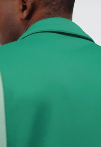 Zelena polo majica s teksturiranim materijalom, koja ima oštar ovratnik i kontrastne šavove duž ramena.